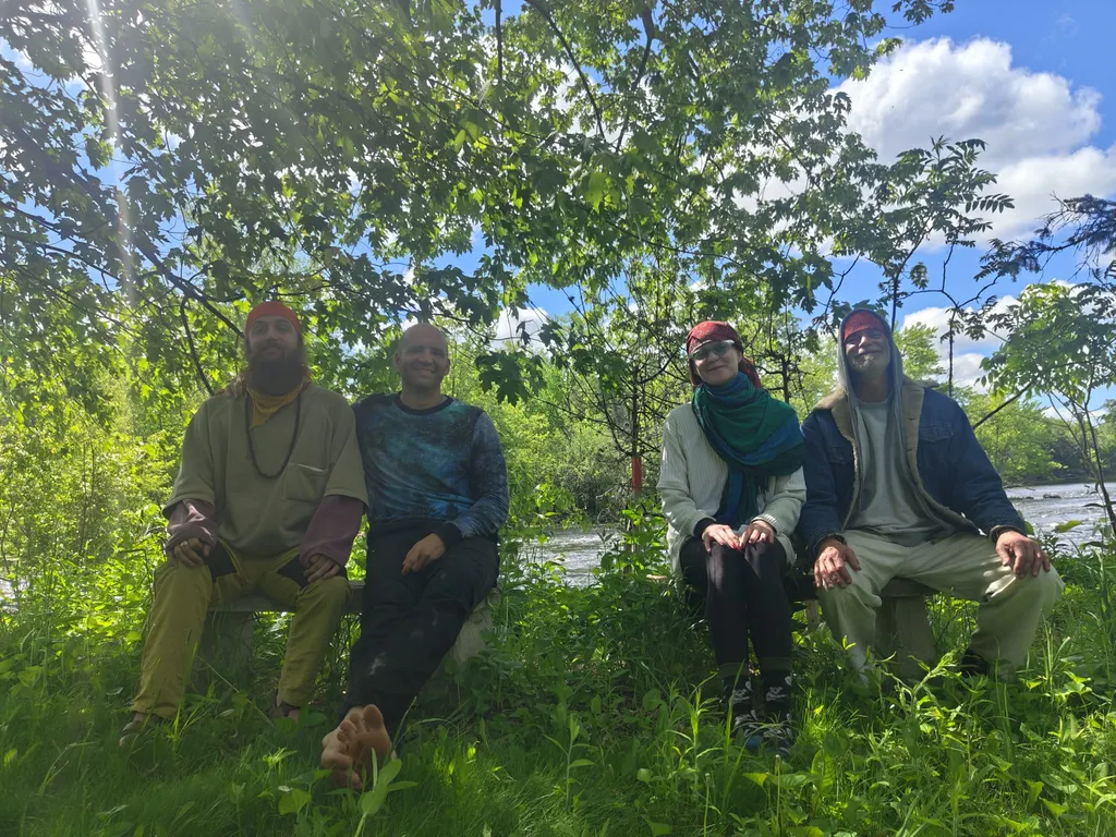 Four members of the collective seated under trees by a river